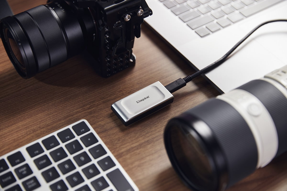 en el centro de la foto un dispositivo de almacenamiento de datos rodeado de un teclado y dos lentes de cámara digital puestos sobre una mesa