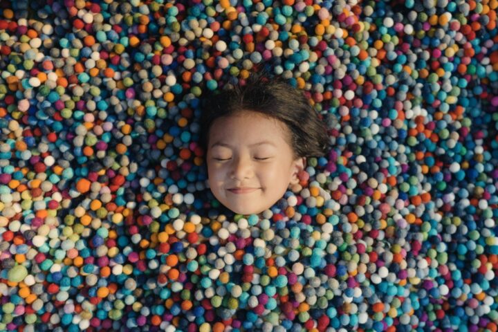 I took this in a felt ball factory while I was shooting a documentary video. This small girl was curious about my camera, so while I was on a break I took her picture. I saw these felt balls lying on the ground and had the idea to photograph the little girl there, coveredwith the colourful material and asking her to close her eyes as if she were asleep.